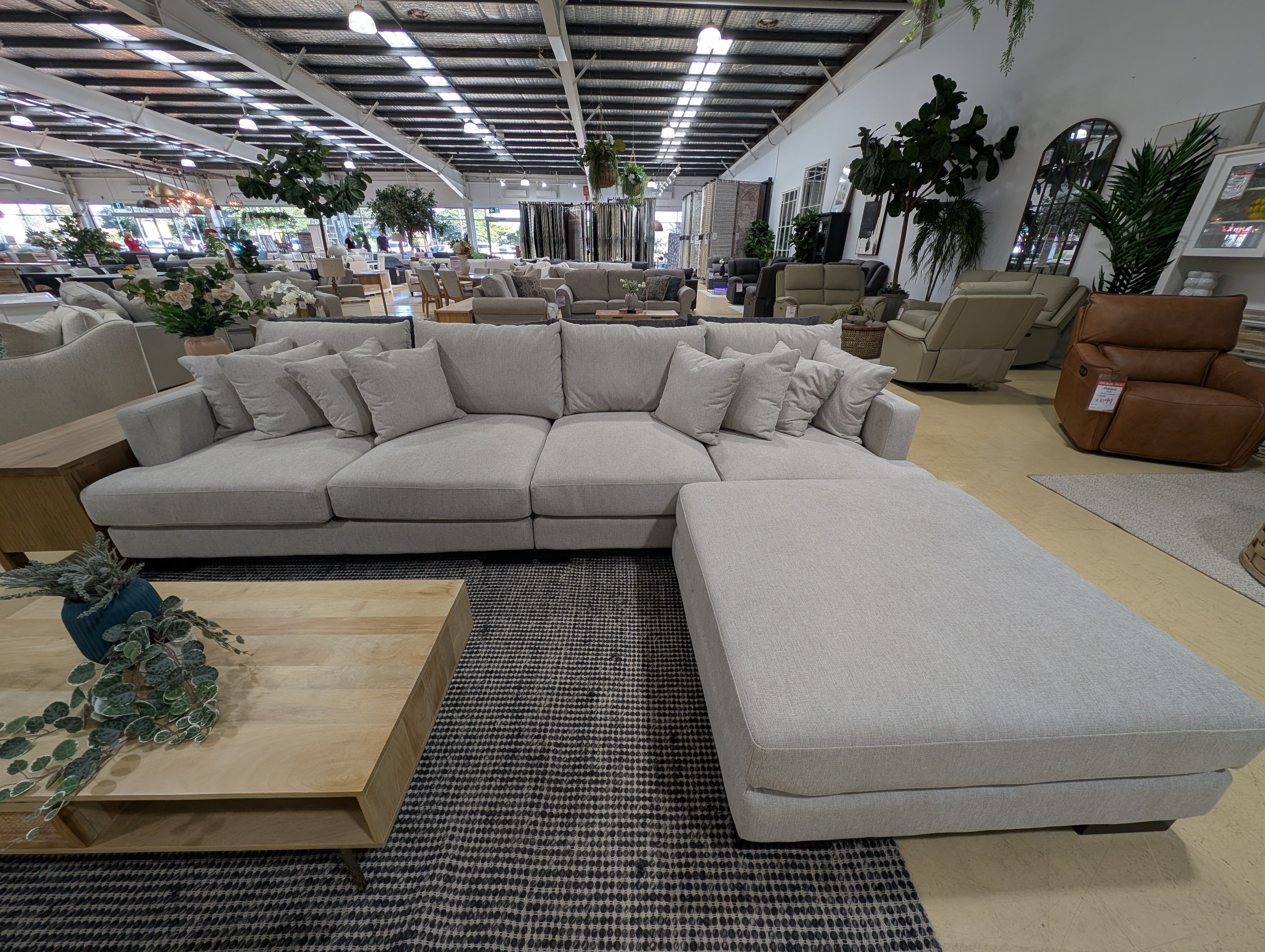 Large gray sectional sofa in a furniture store with various other furniture pieces and decor.